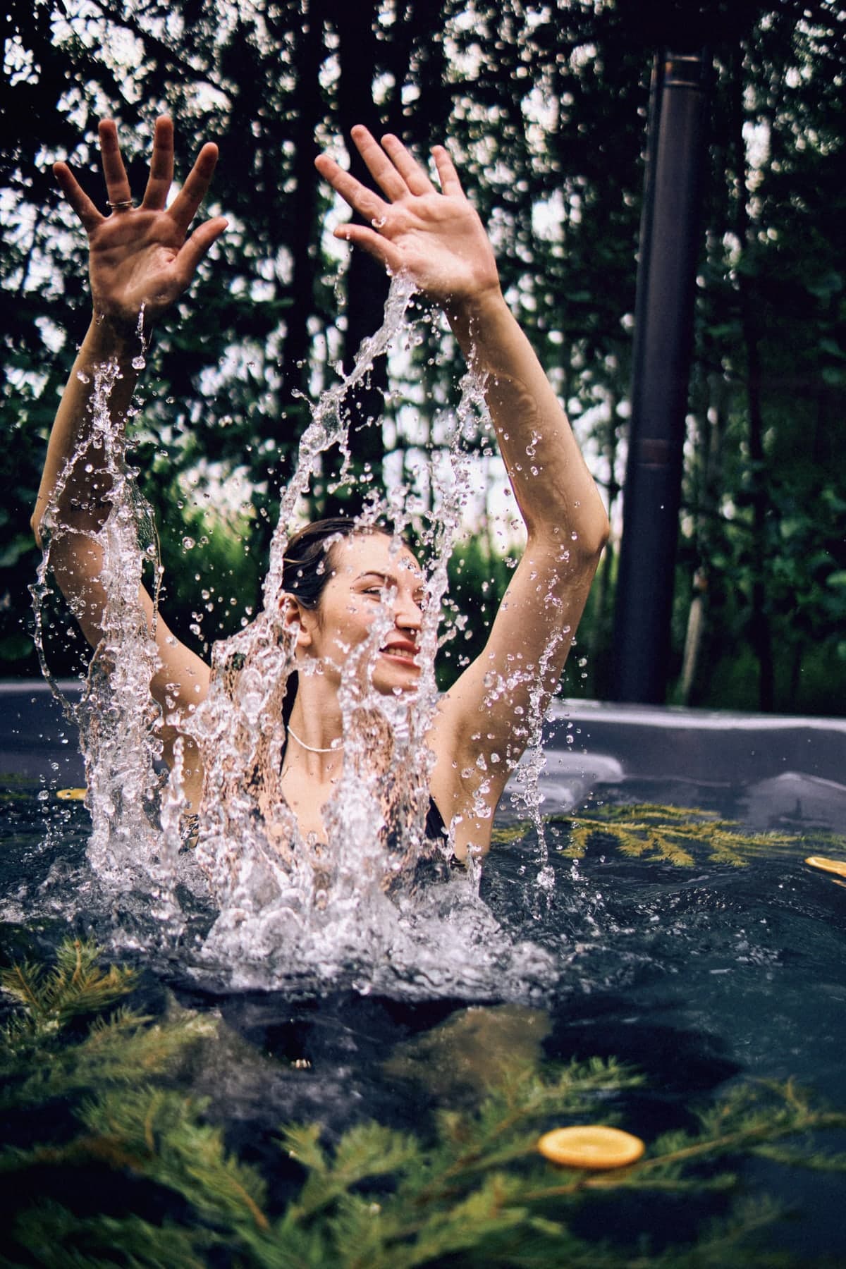 A woman splashing in a hot tub with spruce and orange slices