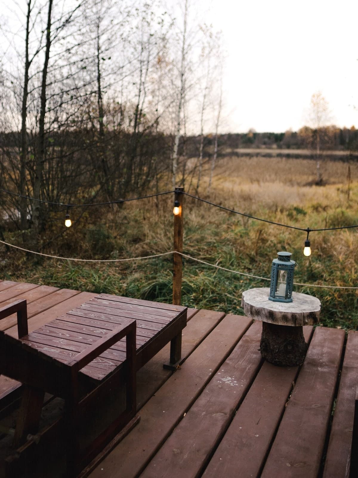 The bathhouse terrace at dusk: string lights and a lantern above an autumn field