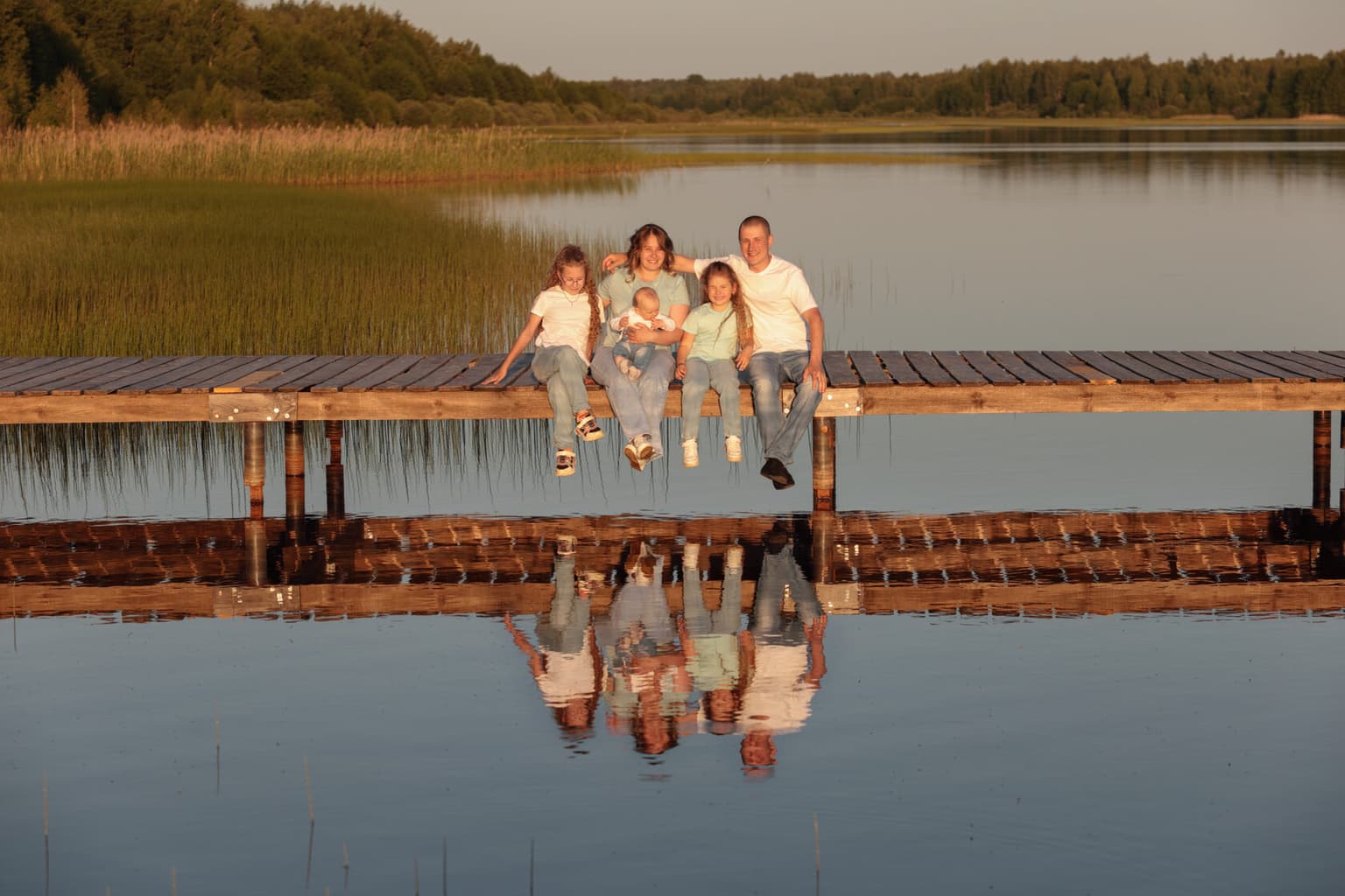 A family with children sitting on the edge of a pier, reflected in the water