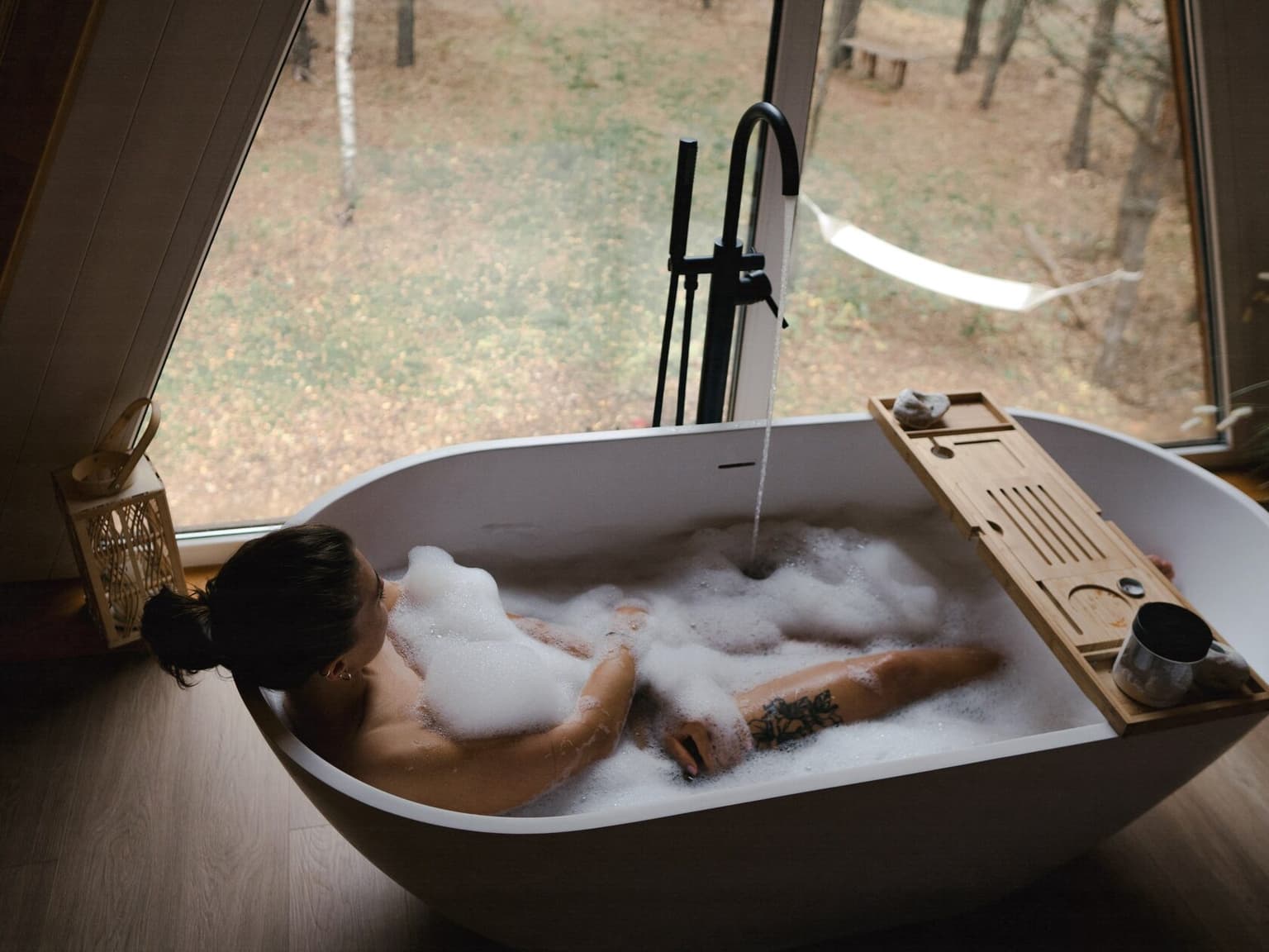 A woman in a bubble bath by a panoramic window