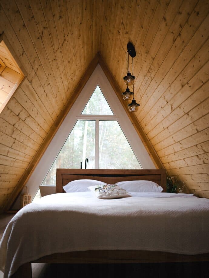 Bedroom under a wooden roof with a window onto the forest