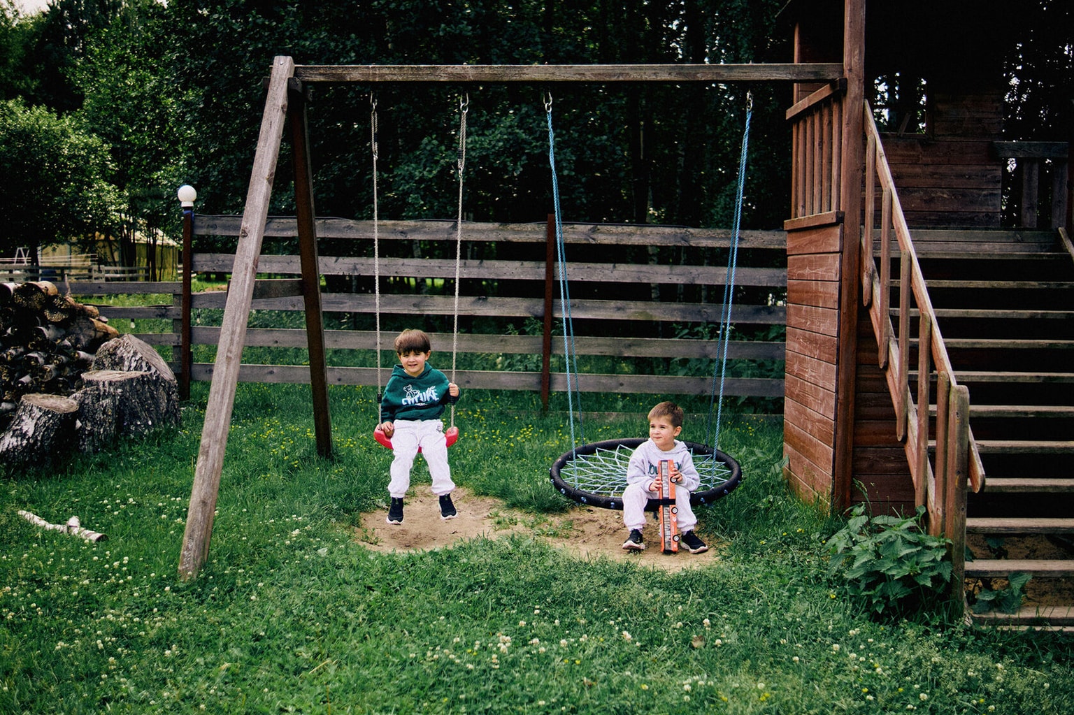 Two children on swings at a wooden playground