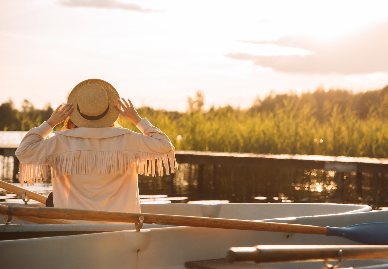 A woman in a straw hat sitting in a boat at sunset